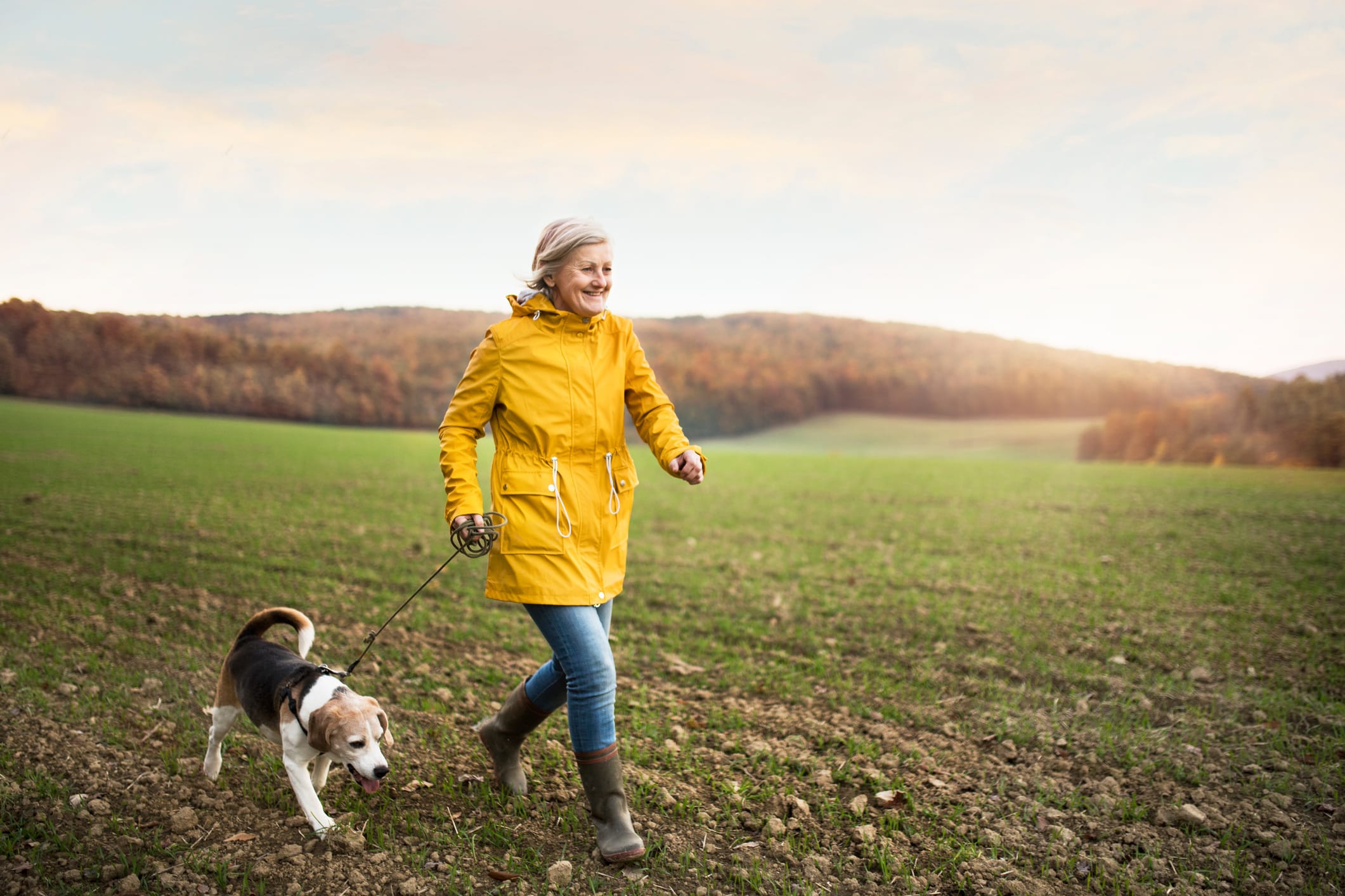 Joyful and financially confident woman taking her dog for a walk in a field
