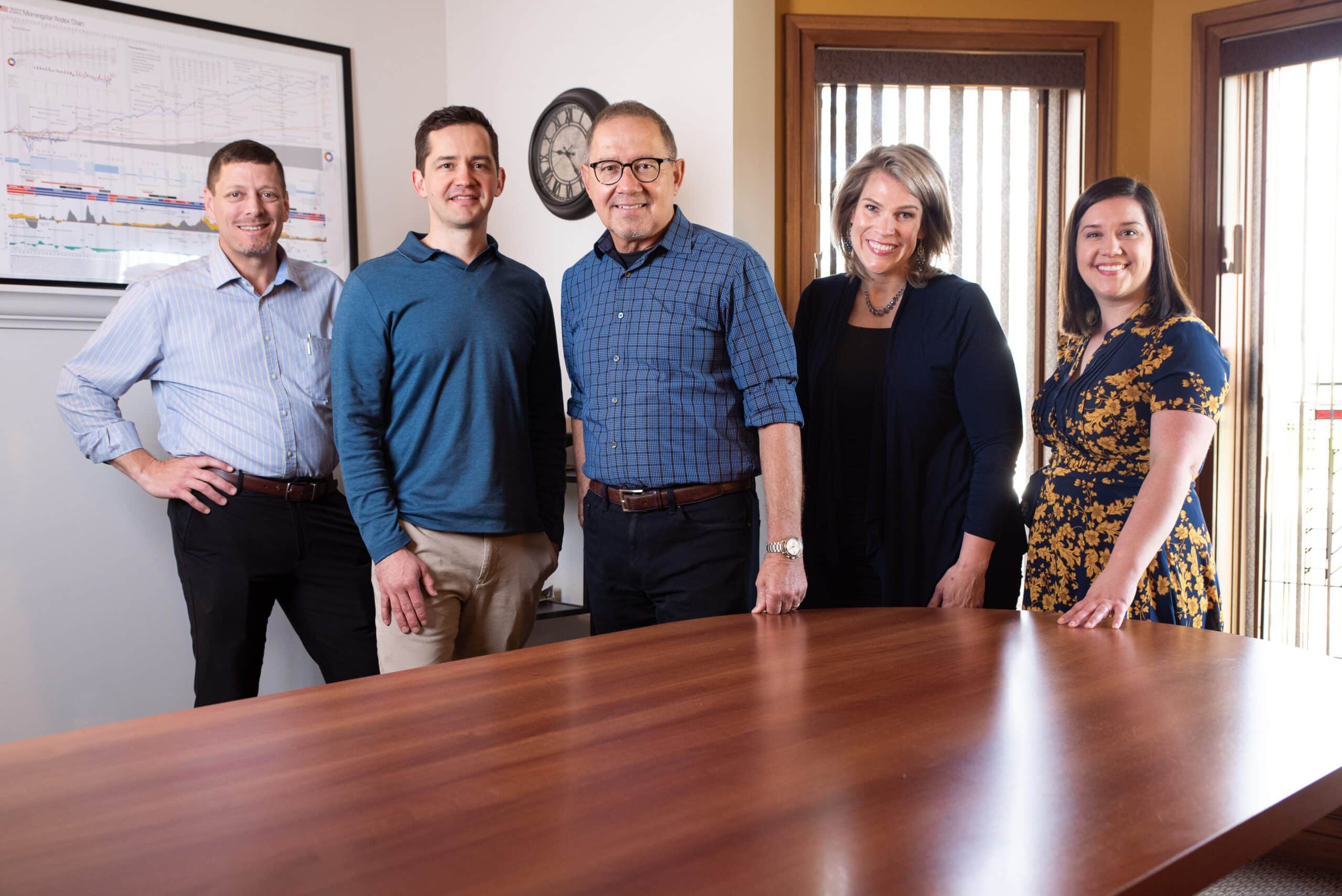 Team of certified financial planners and certified investment management analysts standing around conference room table in the Pleasant Wealth Canton office