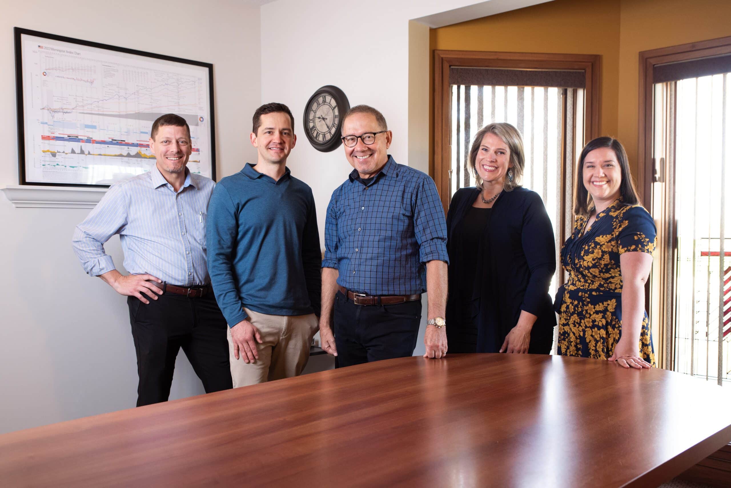 Team of certified financial planners and certified investment management analysts standing around conference room table in the Pleasant Wealth Canton office